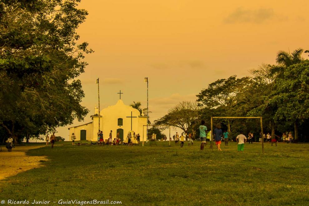 Imagem do entardece e menino jogando bola no campo de grama.